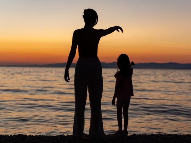 Two figures silhouetted against a sunset over water, one pointing out to sea.